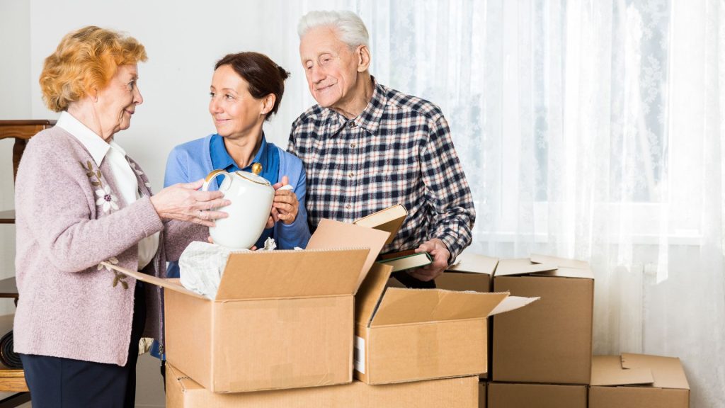 three people standing in a living room with boxes